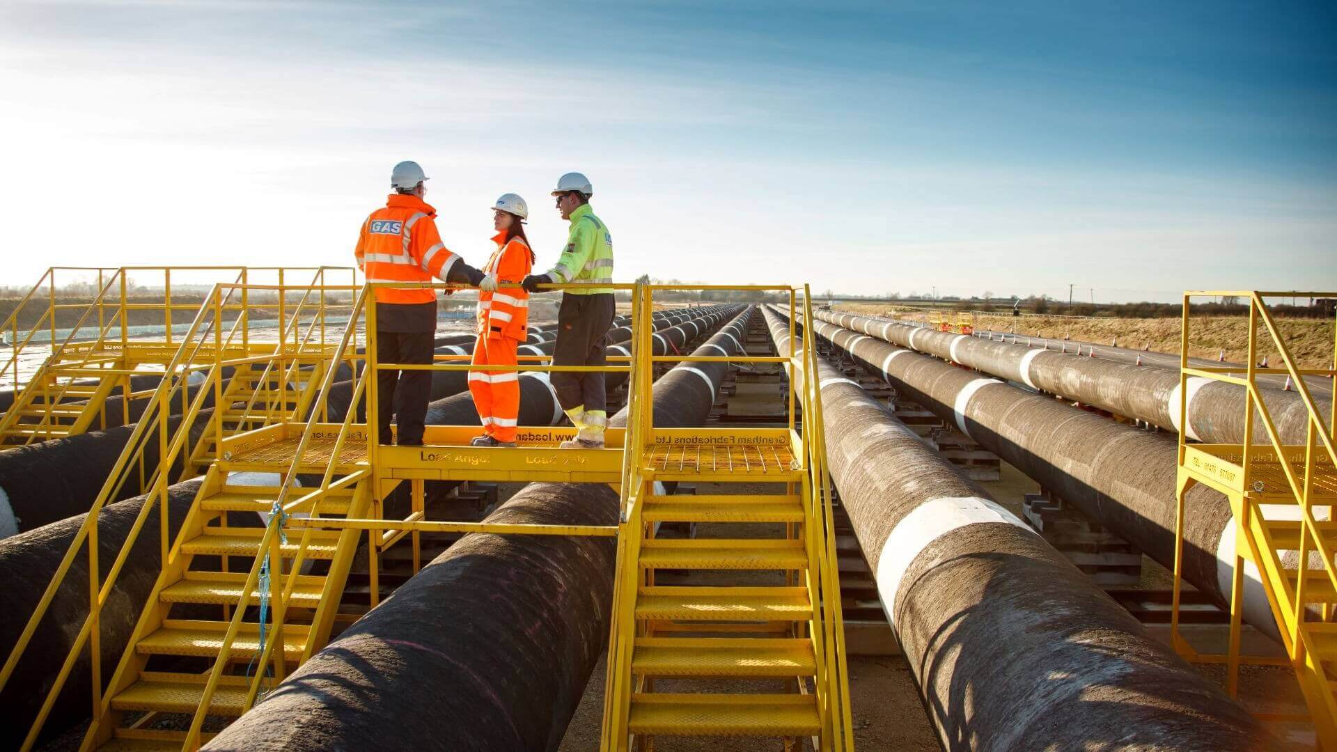 Three engineers stood on platform over rows of gas pipelines