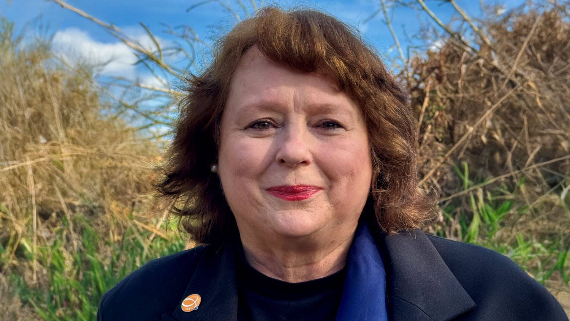 Head and shoulders photo of Diana Davidson, standing outside, in front of hedgerow