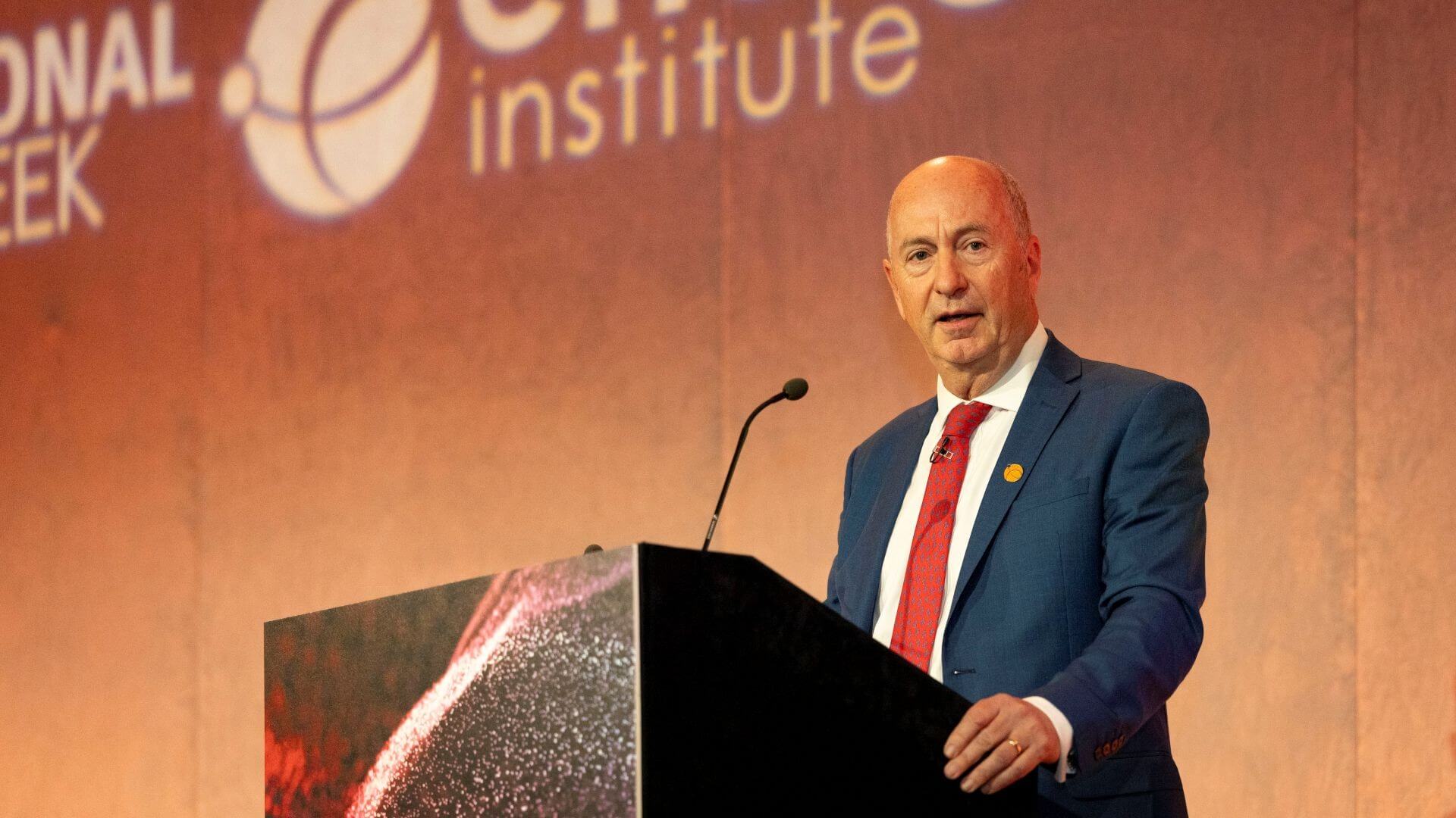 Head and shoulders photo of Andy Brown standing behind a lecturn, speaking to conference delgates