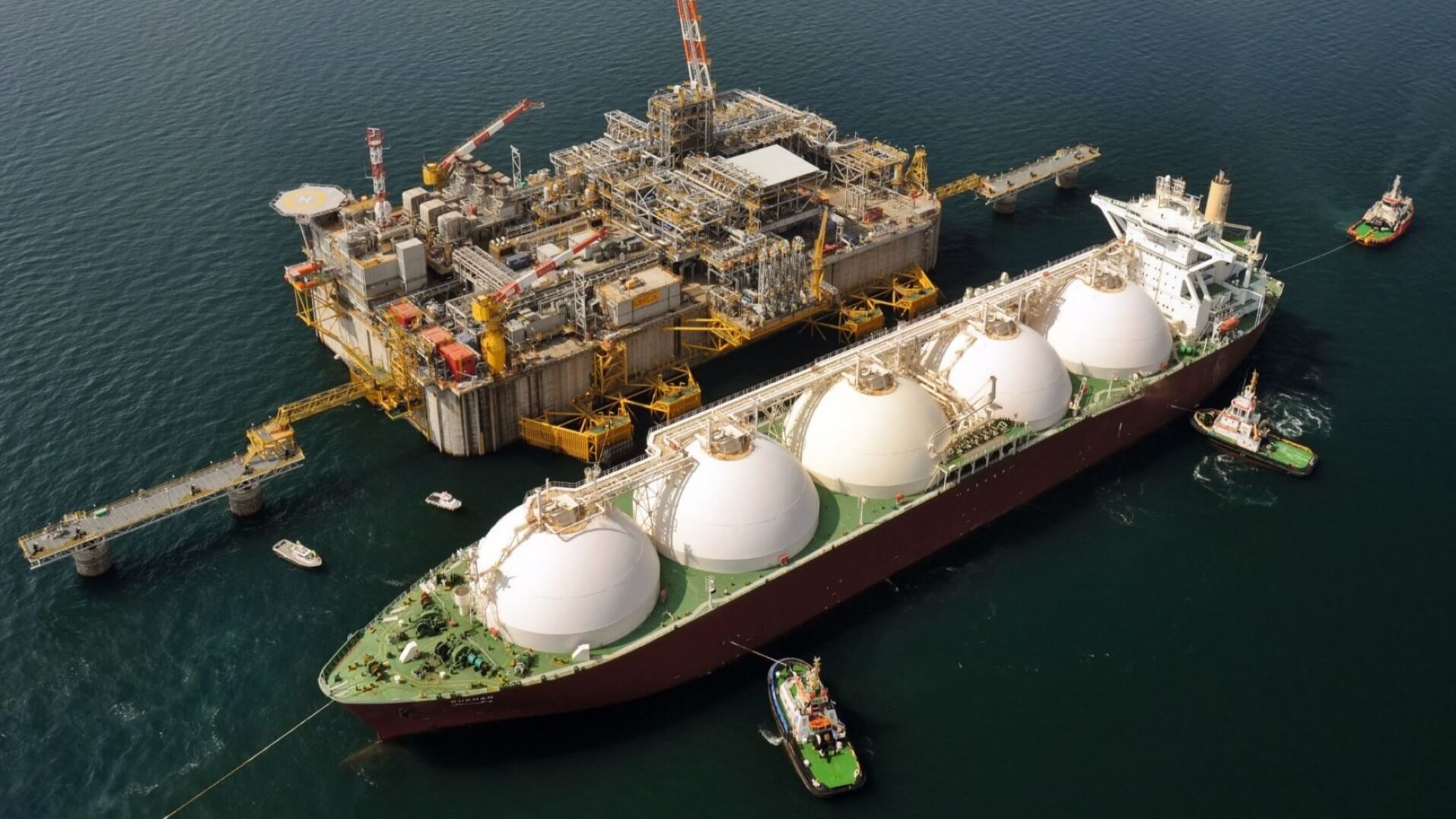 Aerial photo of LNG tanker alongside offshore processing platform, with tugs boats holding it in position