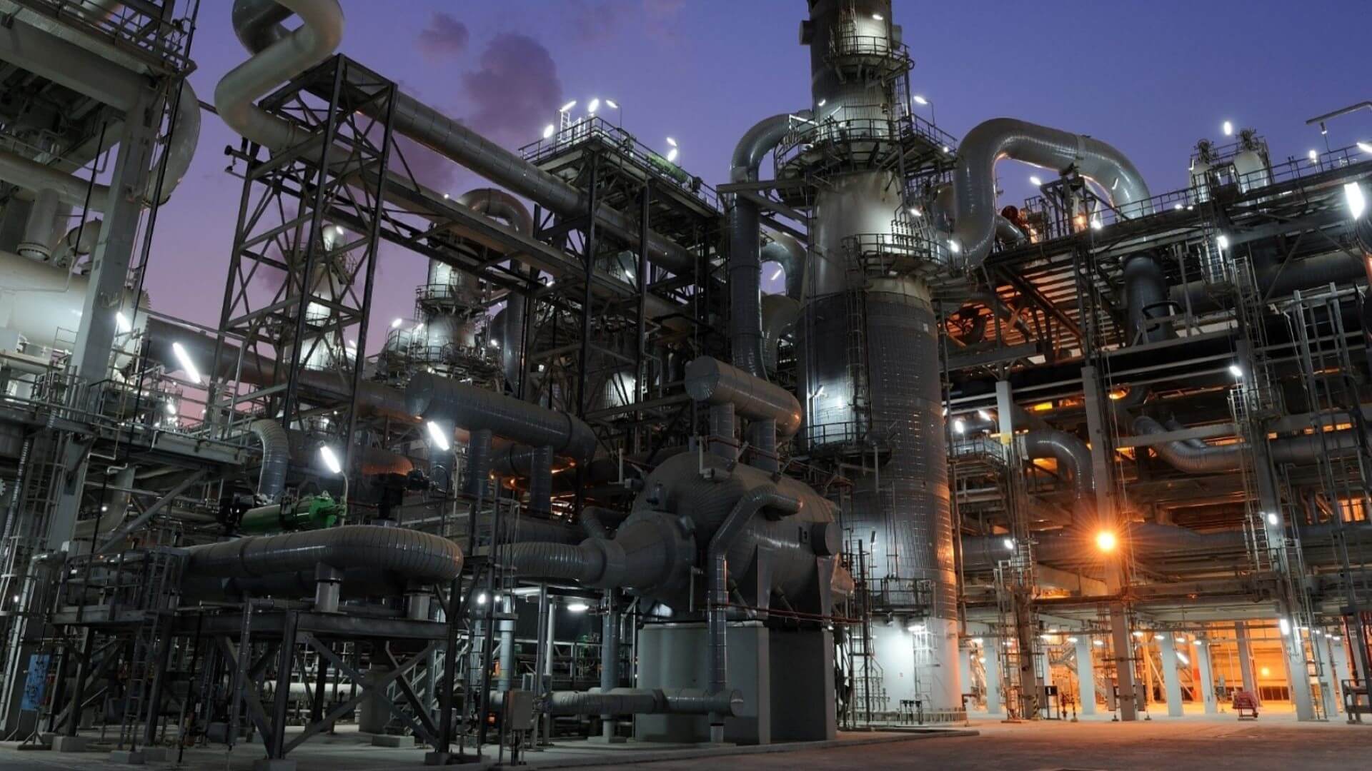 View of gas processing plant lit up at night - close up of pipework, cylindrical tanks and gallery walkways