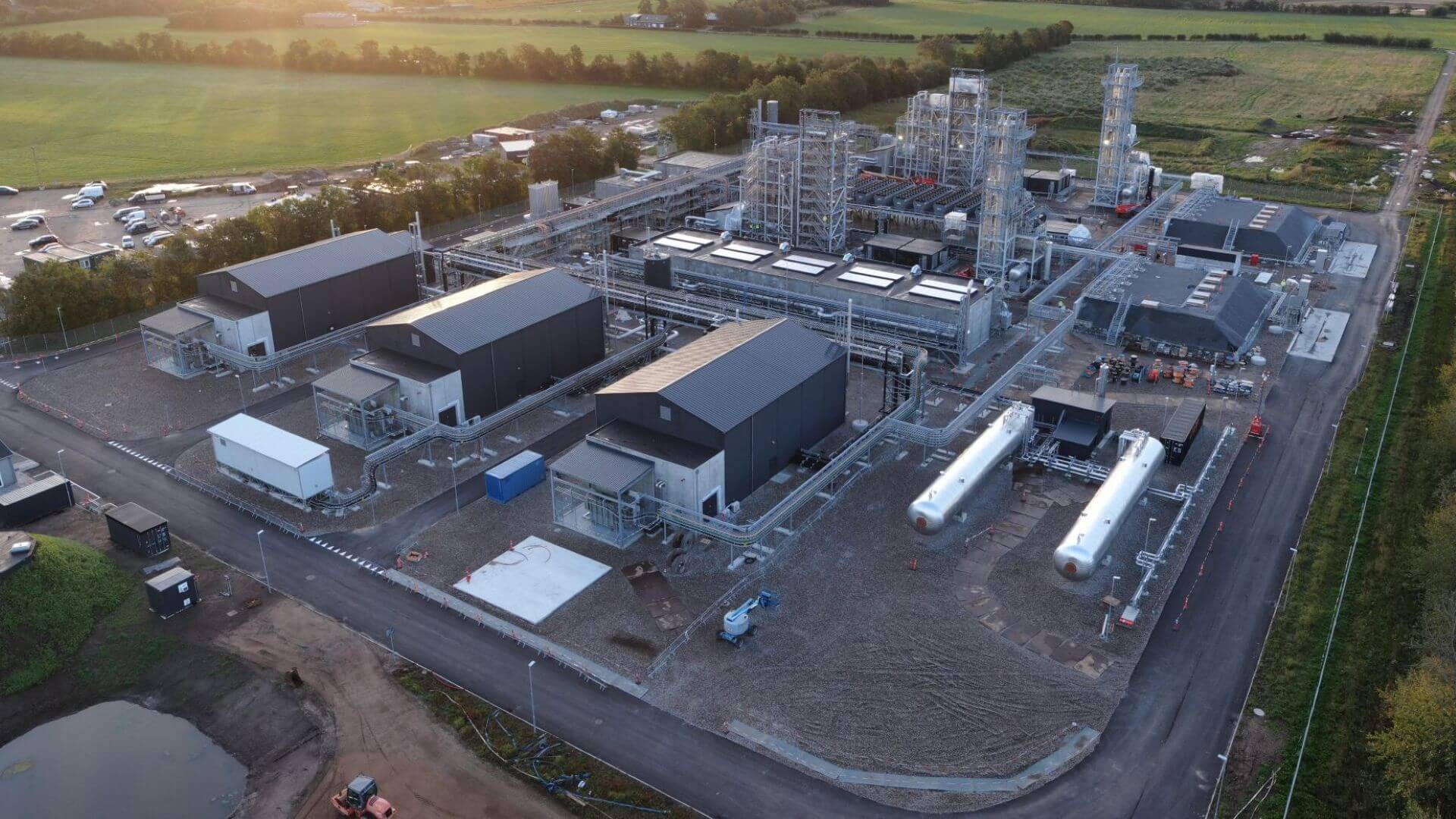 Aerial view over power-to-x project showing rectangular industrial plant buildings, long cylindrical storage tanks and towers of pipework