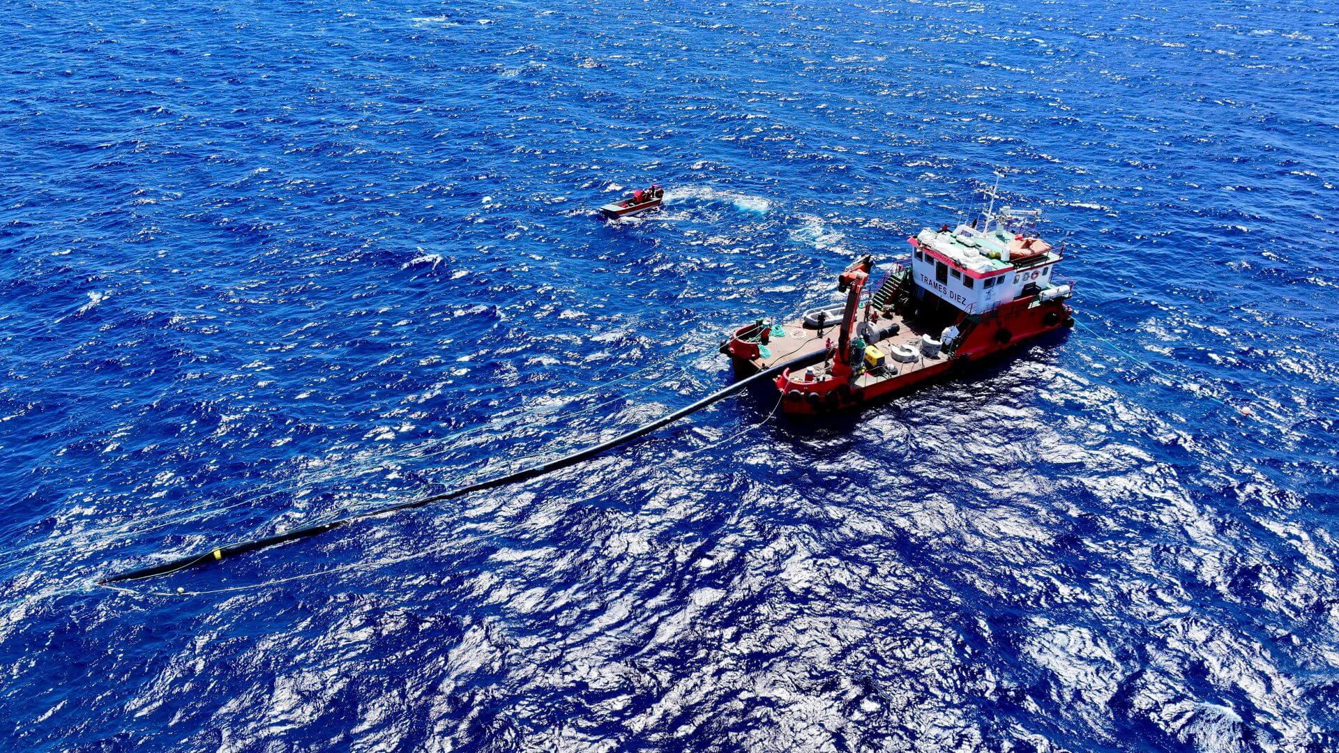 Aerial view of vessel at sea towing a pipe behind it