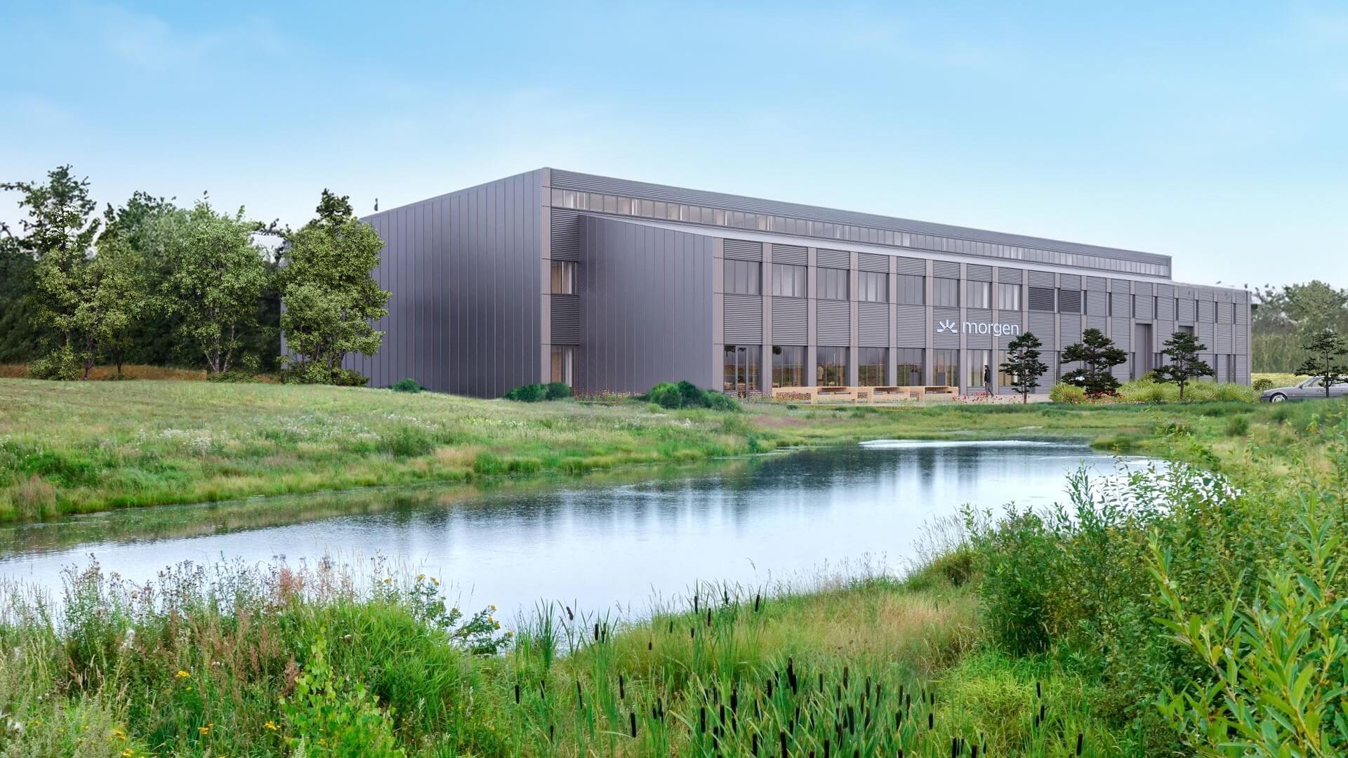 Computer generated image of sleek, modern building surrounded by green grass and trees, with a body of water in front