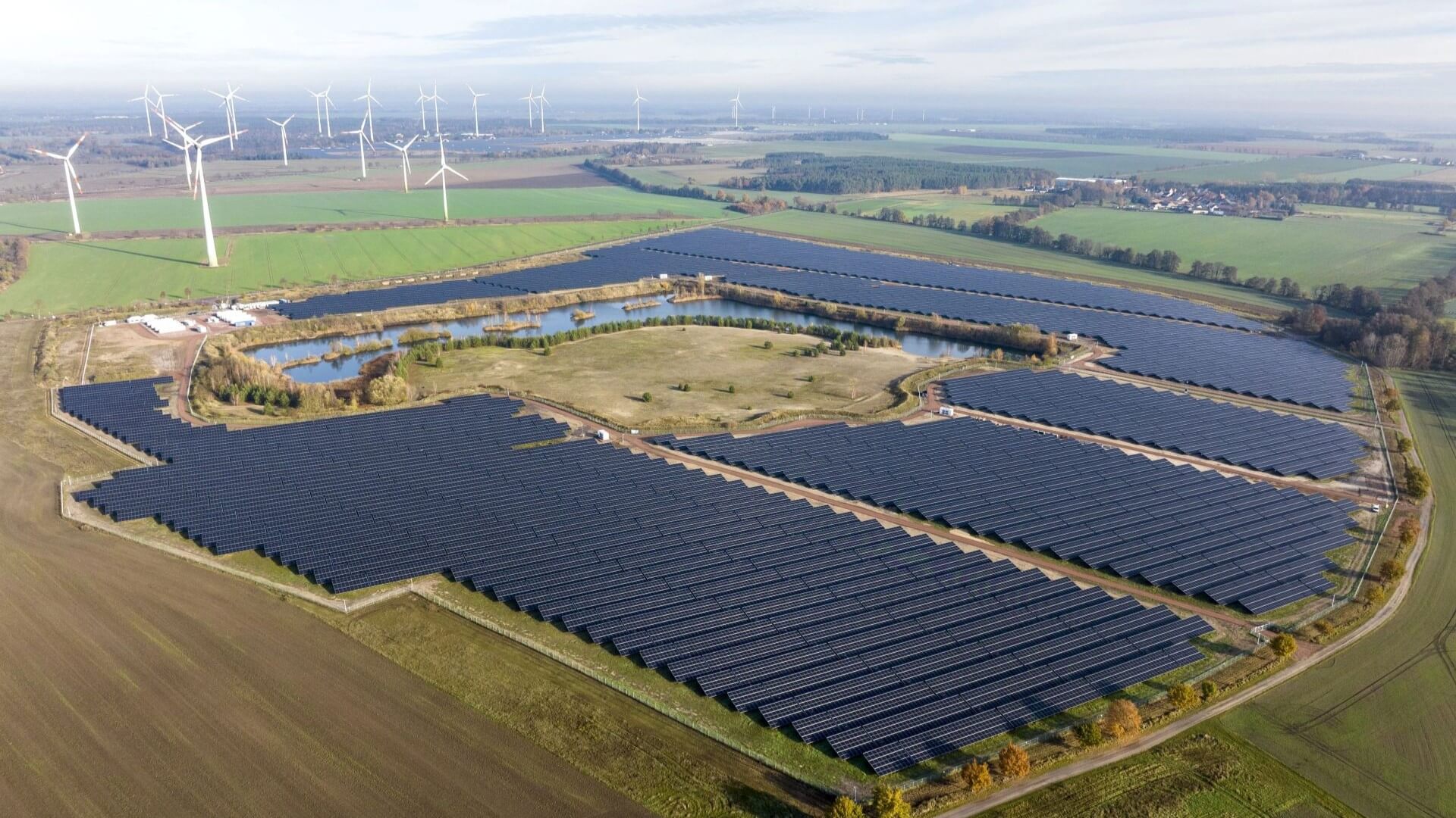 Aerial view over rows of solar panels next to rows of wind turbines, with a square grid of battery energy storage systems between