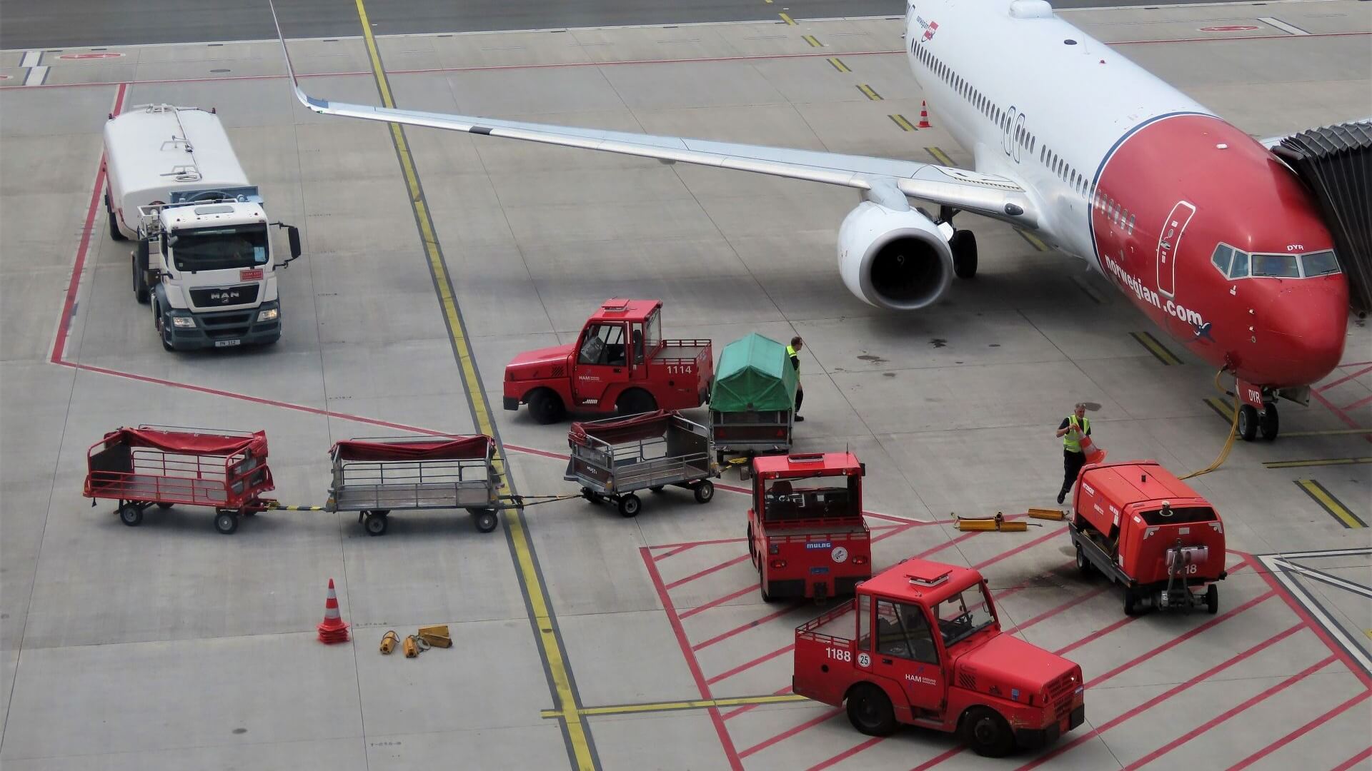 Aeroplane at an airport, with refuelling truck approaching and baggage trolleys and other small airport vehicles nearby