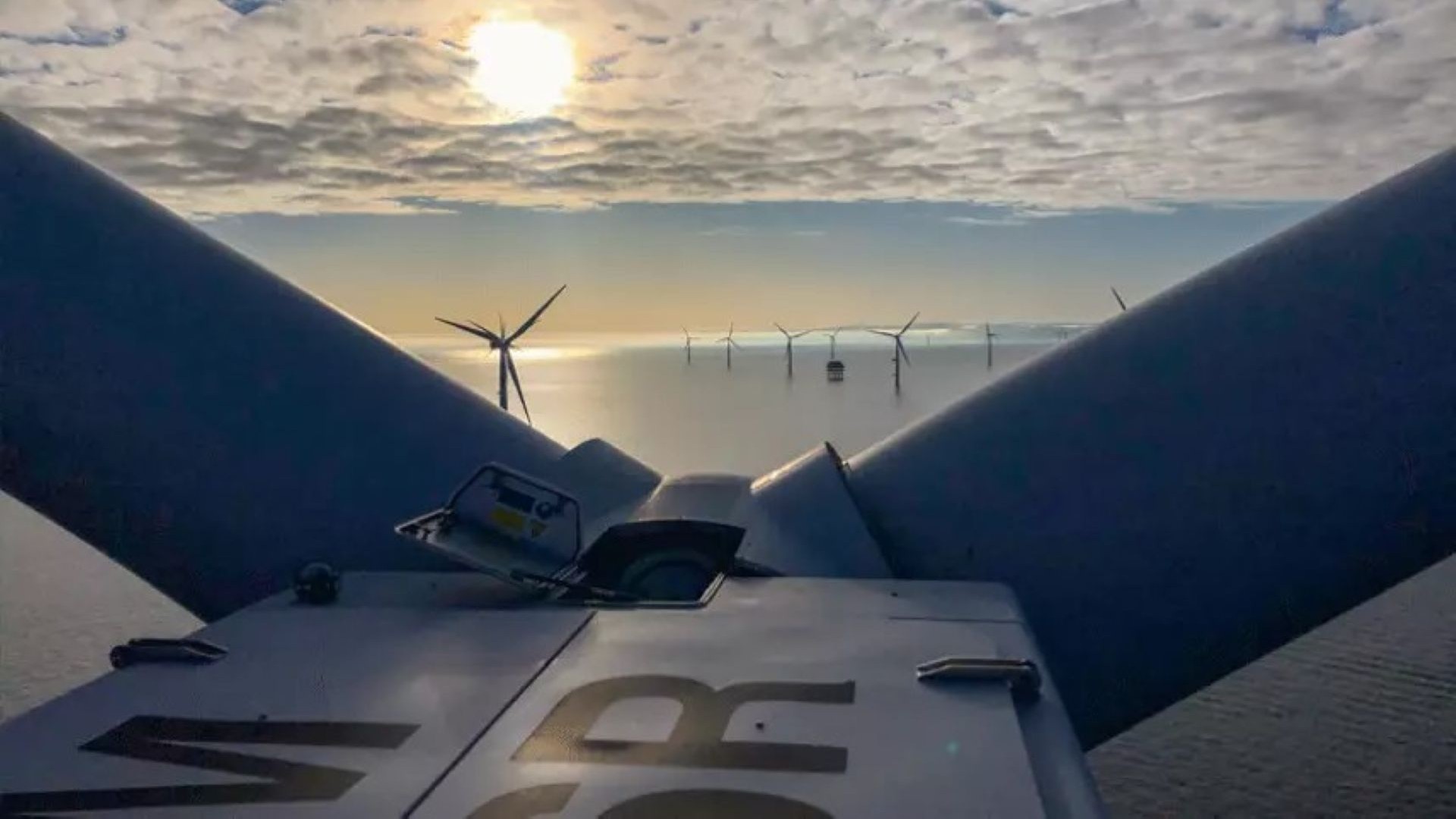 View from the top of a wind turbine nacelle, looking between blades to see wind turbines in distance
