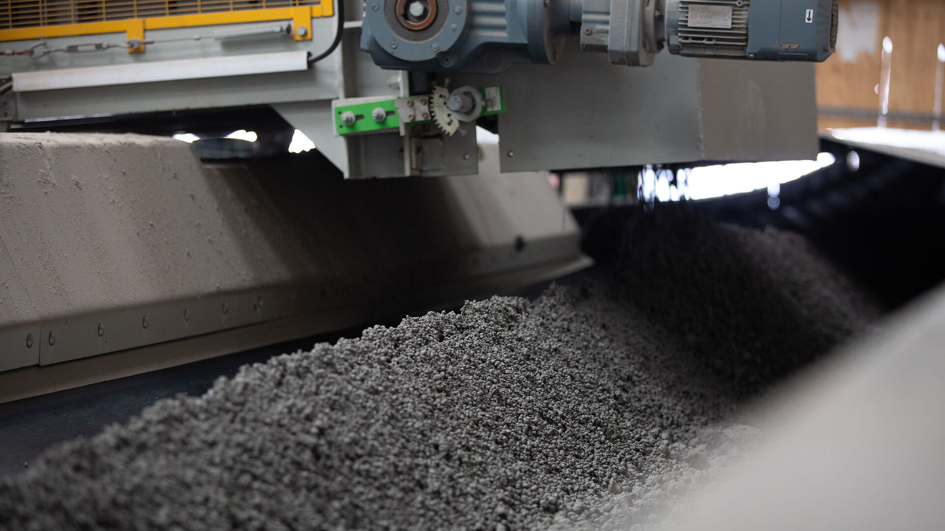 Close up of pile of grey/black coloured granules on a conveyor belt with equipment above
