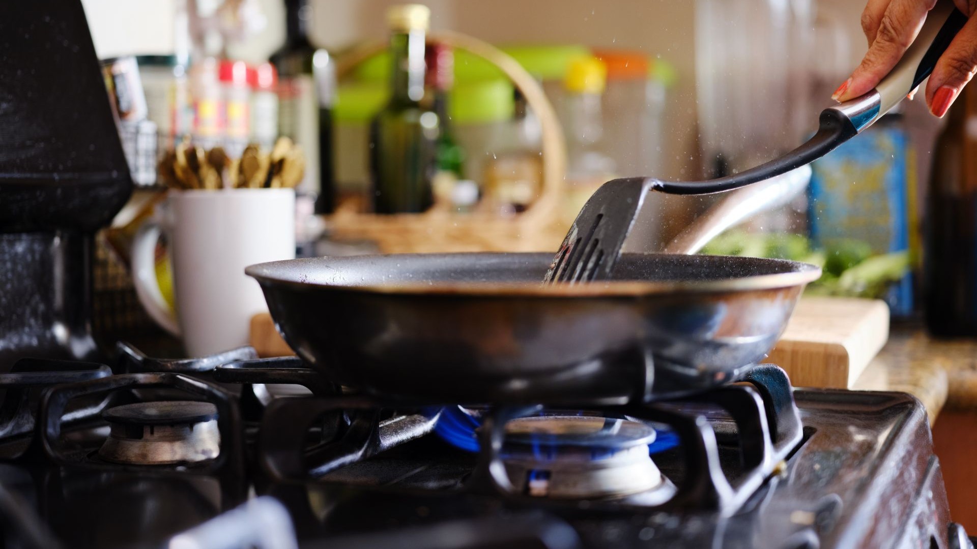 Close up of hand holding a spatular stirring food in a frying pan on a gas cooker hob