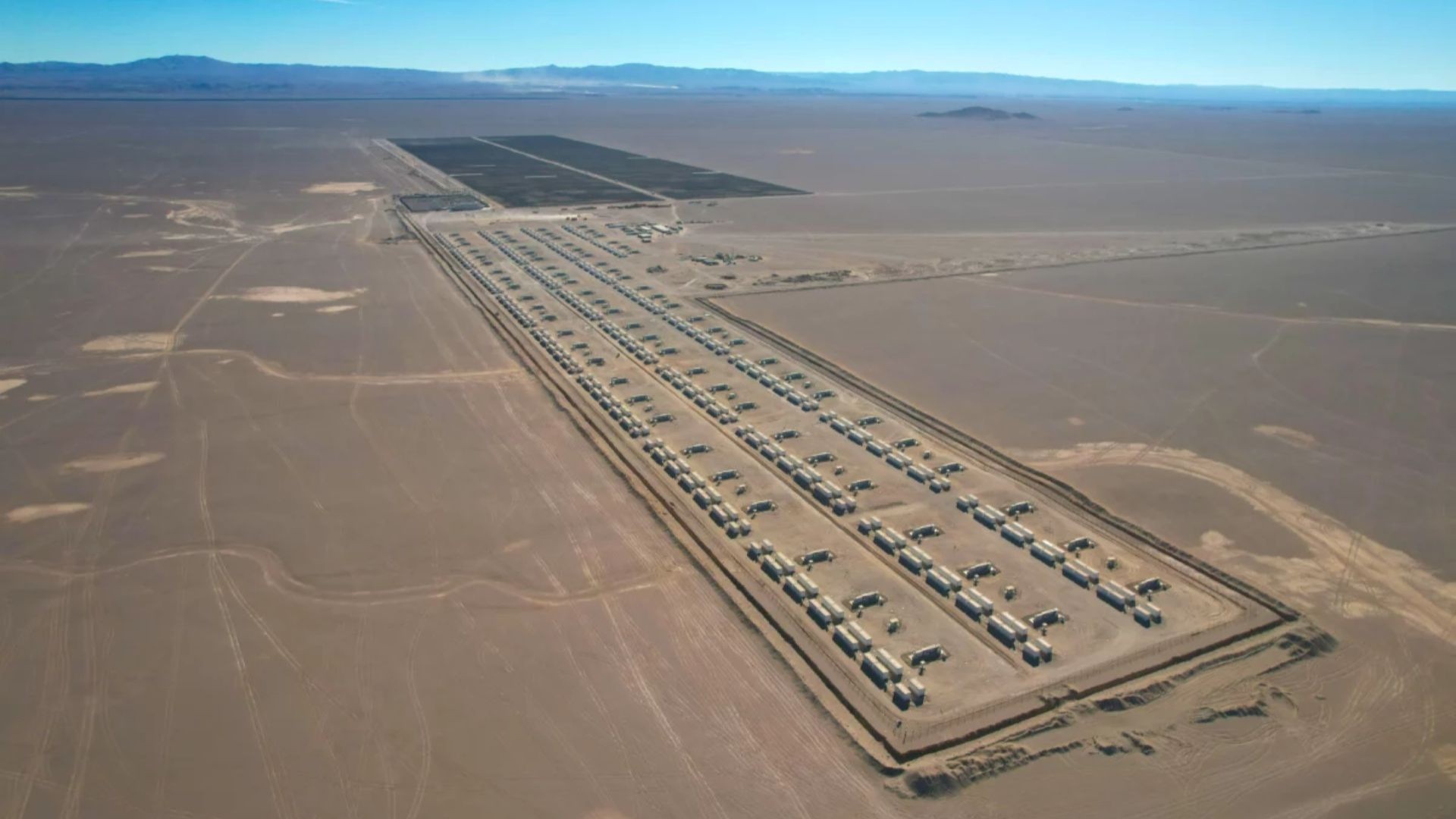 Aerial view over rows of rectangular battery energy storage systems stretching across desert sands