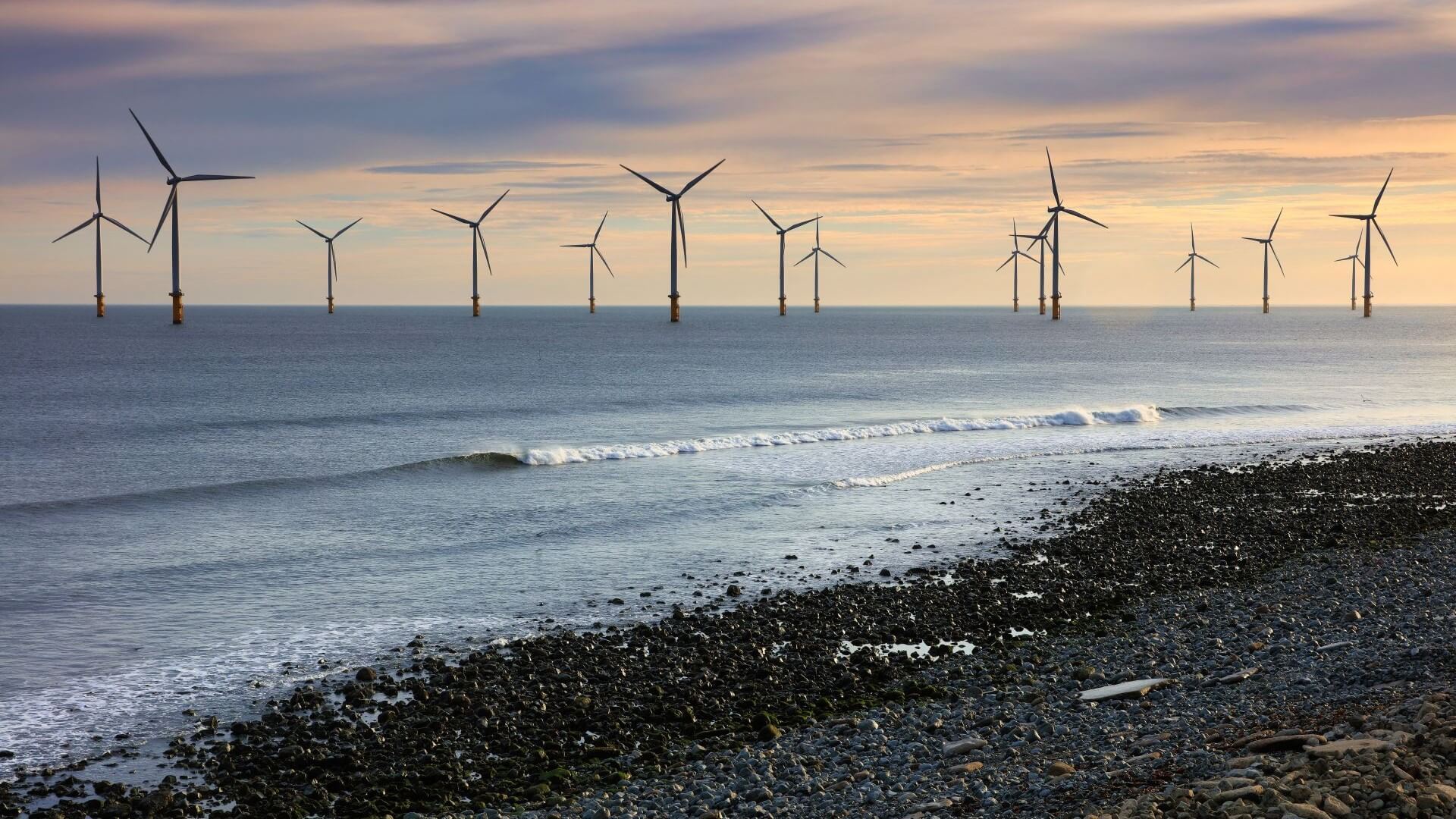 View of rows of wind turbines in the distant horizon, with shingle beach and sea in foreground