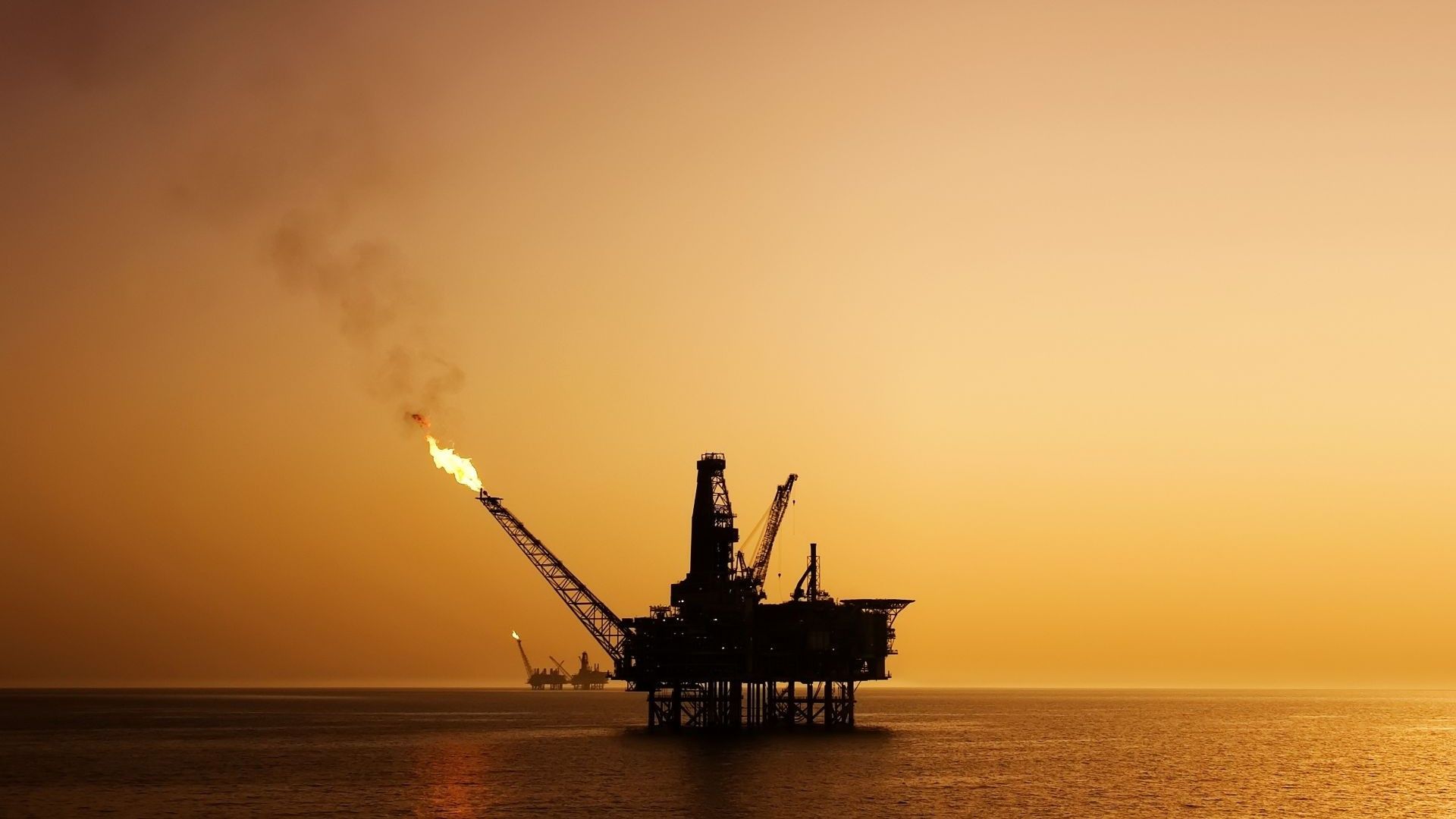 Silhouette of offshore oil platform flaring gas, set against an orange sky