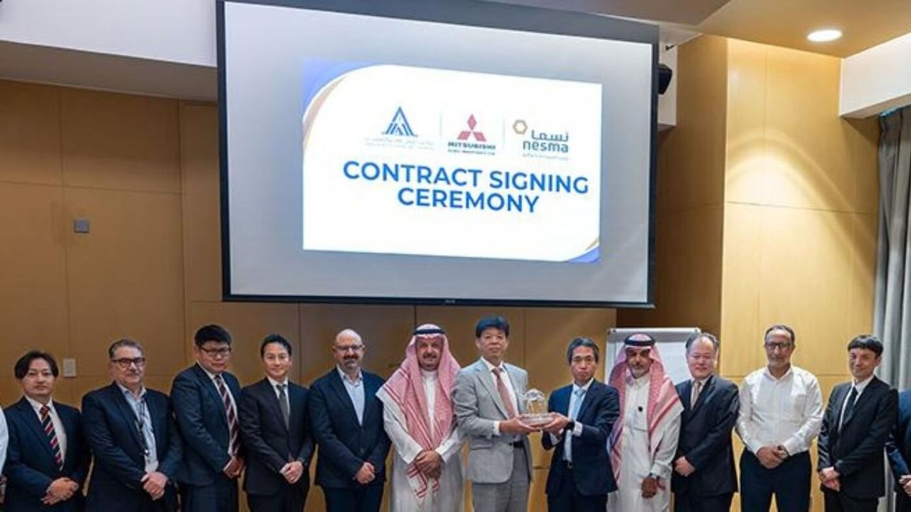 A row of men, some dressed in Middle Eastern robes, stand in front of a large screen projecting the title 'Contract signing ceremony' and company logos