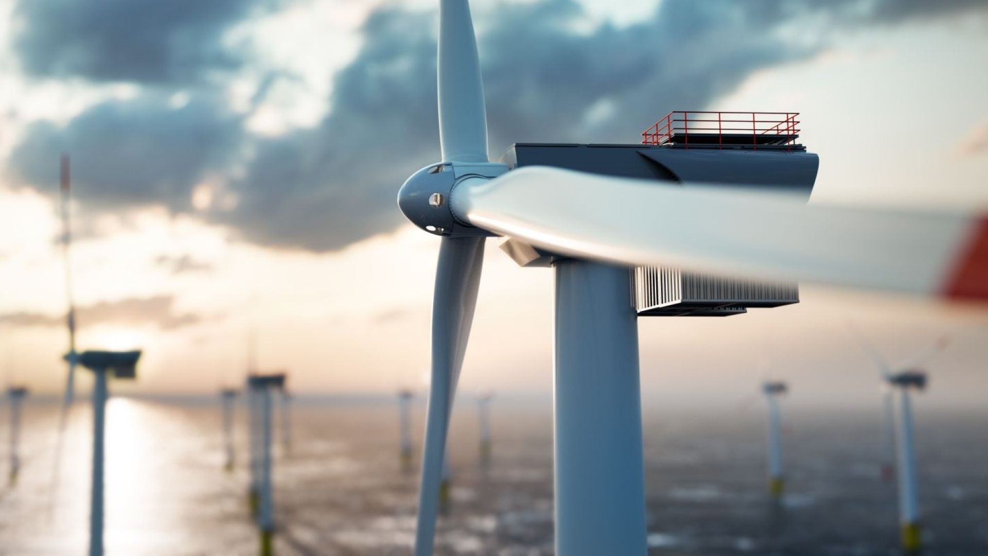 Close up of three blades and nacelle of an offshore wind turbine, with more wind farm turbines at sea in background of image