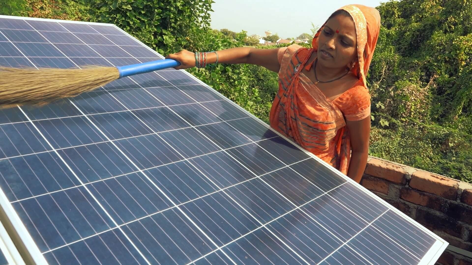 Close up of Indian woman in traditional dress, using a brush to clean the surface of a floor-mounted solar panel