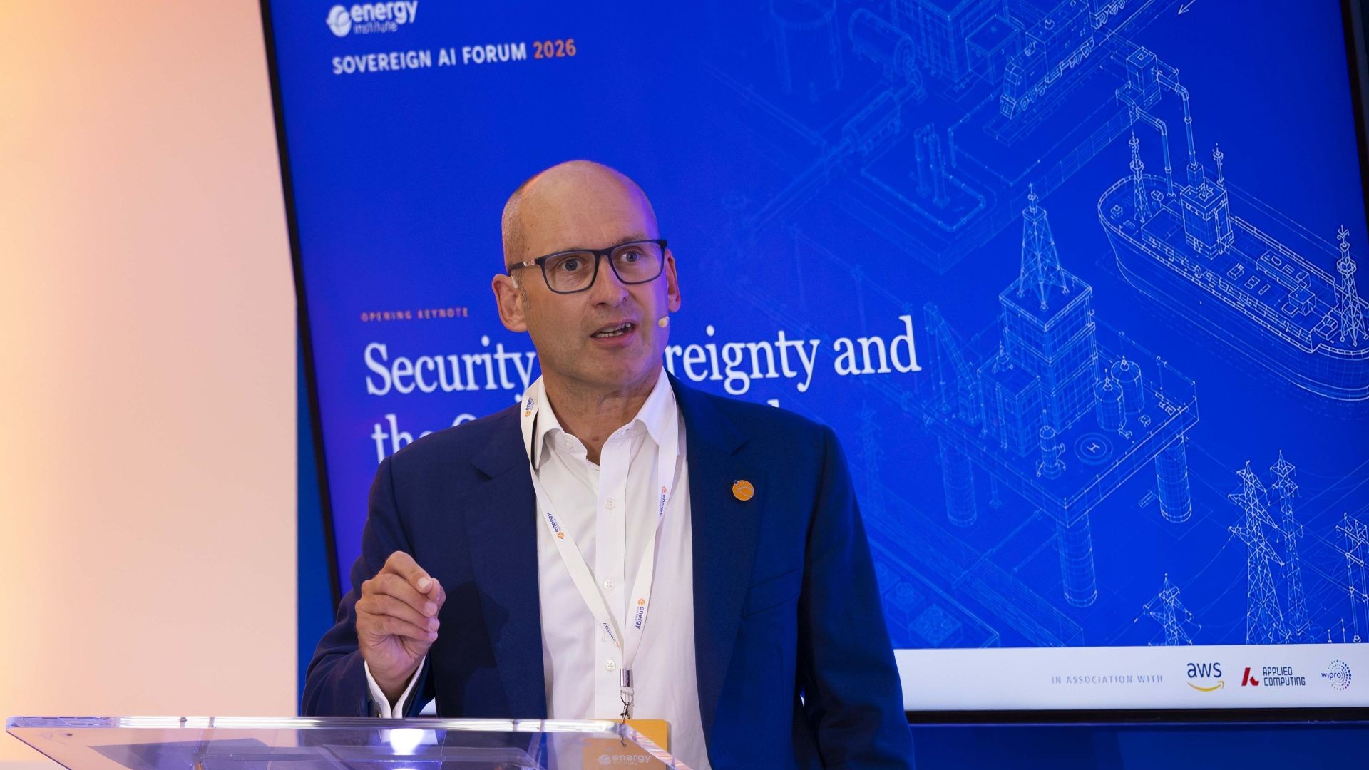 Energy Institute CEO Nick Wayth standing behind a clear perspex lecturn, with right hand raised to make a point to delgates, with projection screen behind showing presentation title