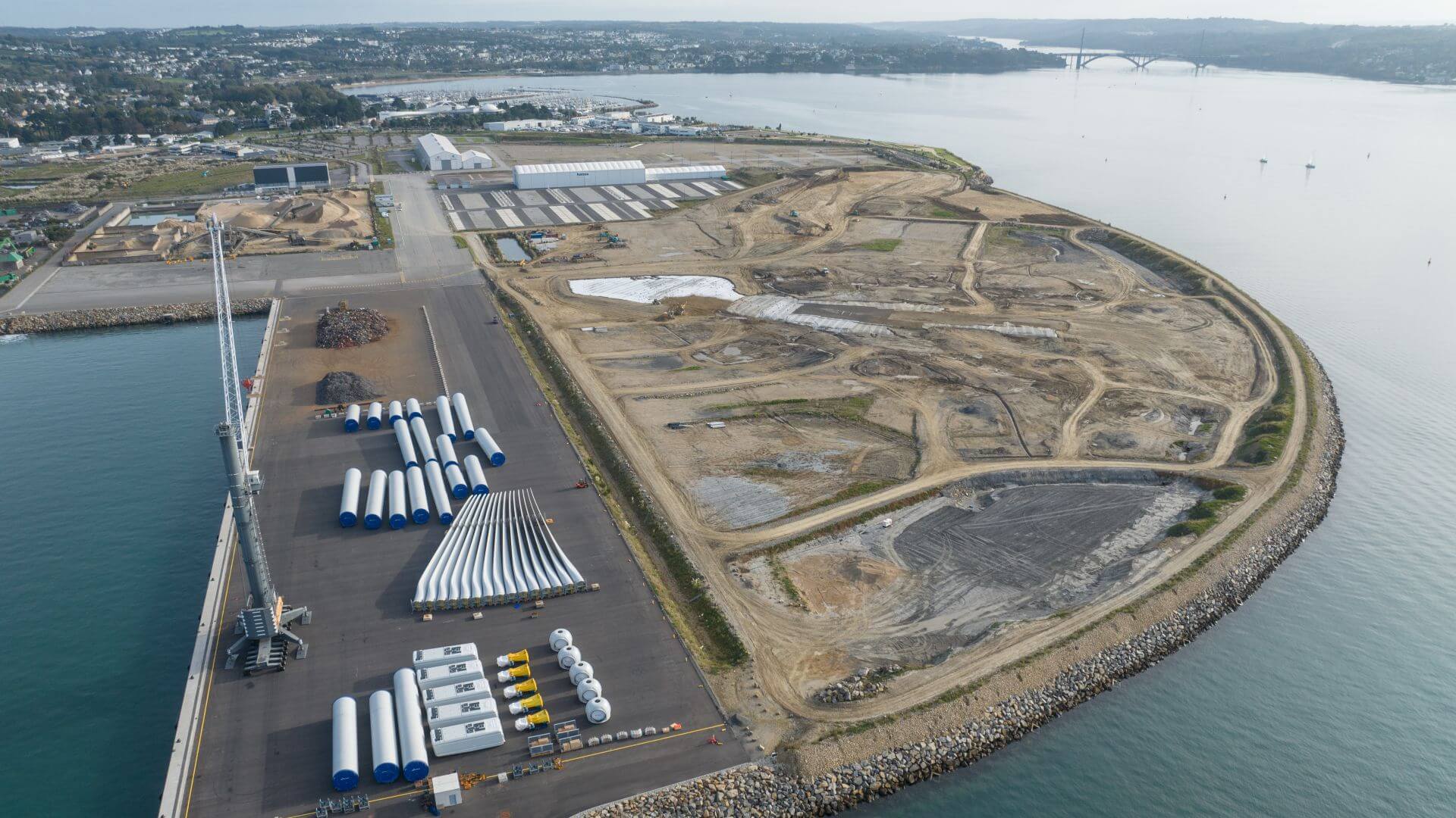 Aerial view of port area with wind turbine comopoents, including tower sections, blades and nacelles, laid out on the ground awaiting transport to offshore assembly site
