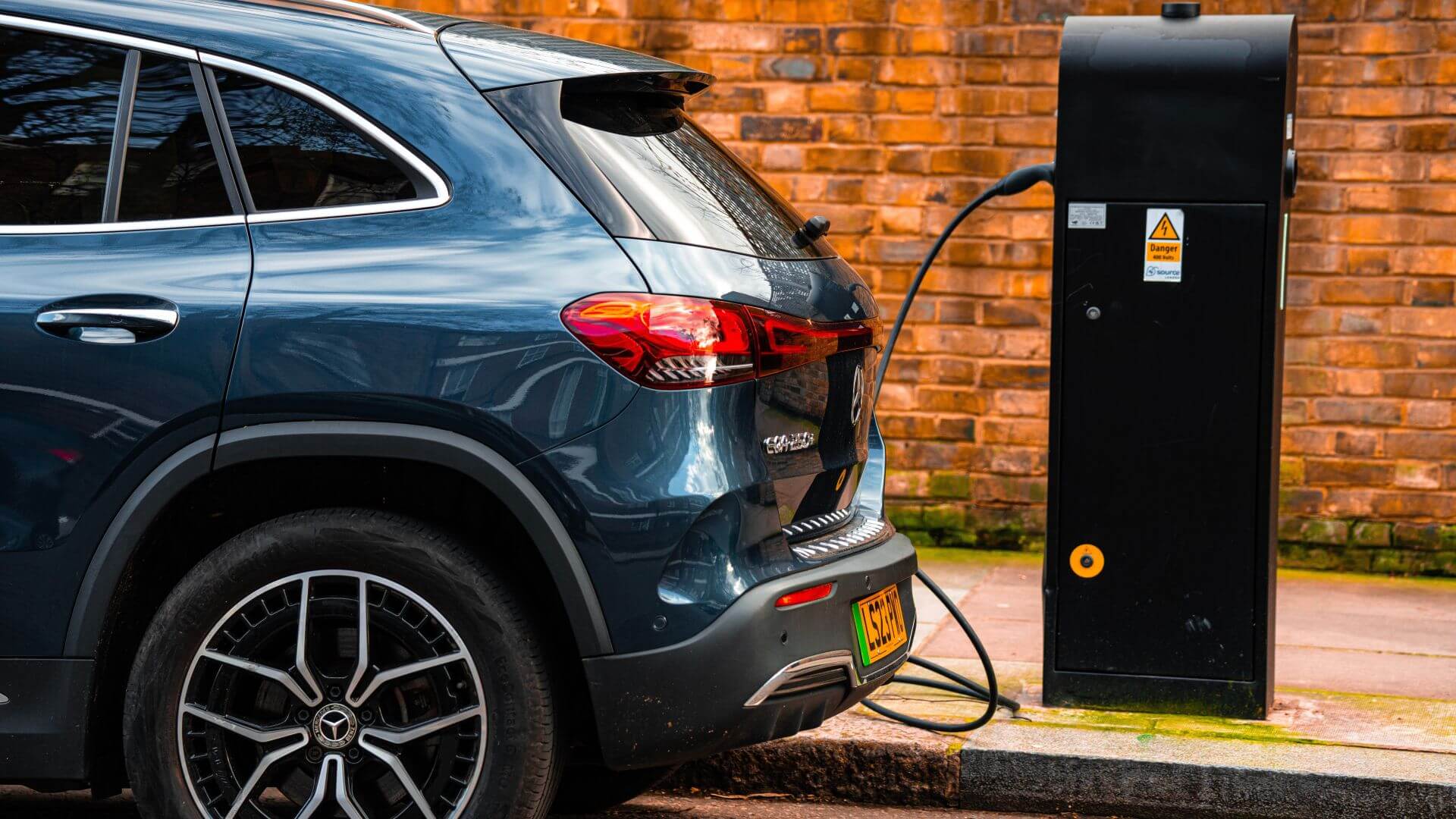An electric car parked on the roadside, plugged in to a charging unit set on the pavement
